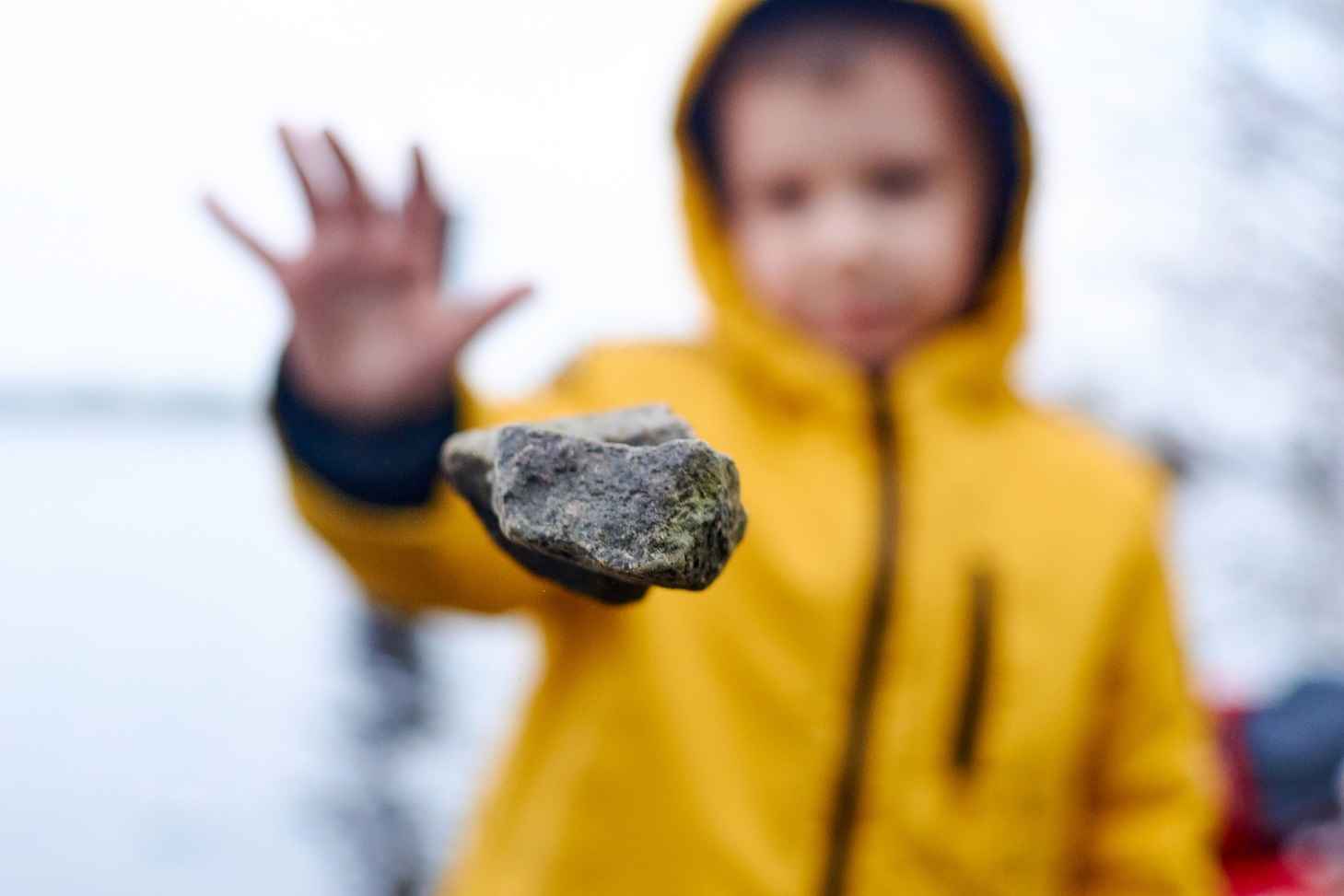 Kid wearing yellow jacket is throwing a stone in the air.